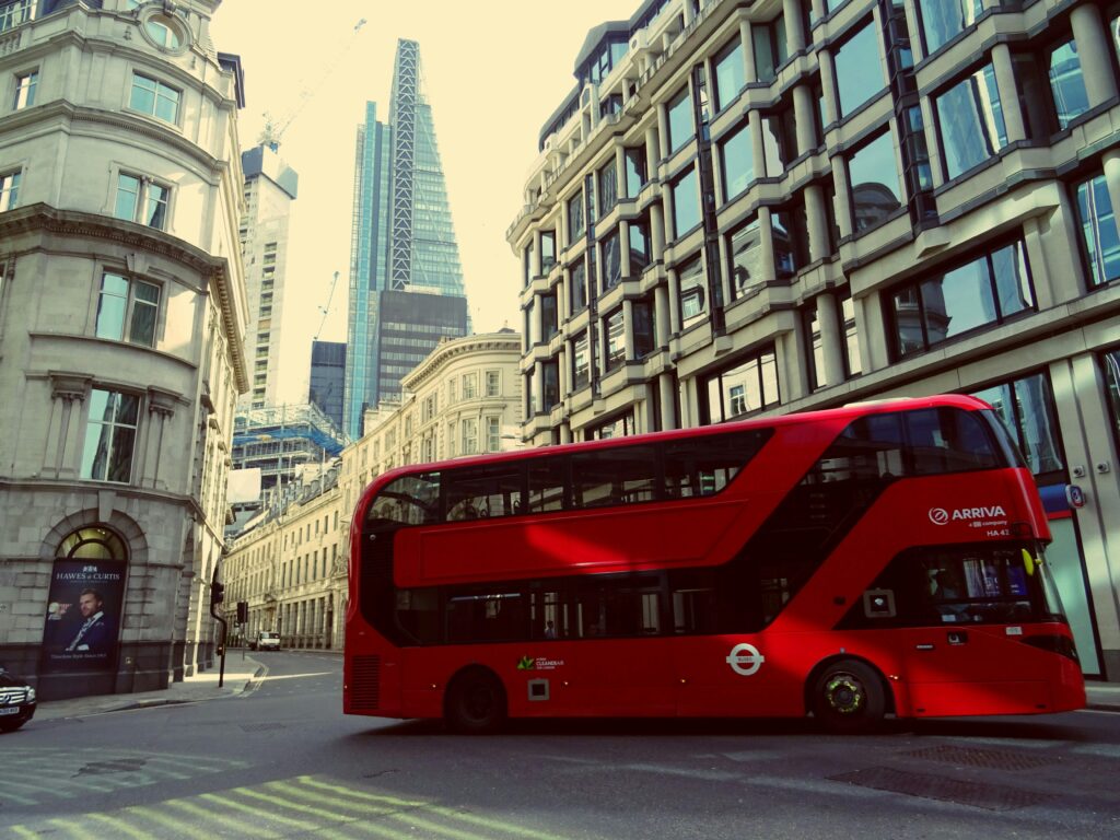 Vibrant red double-decker bus cruising through London's busy city streets with iconic architecture.